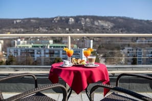 Une table recouverte d’une nappe rouge sur un balcon, avec une vue sur la ville et des montagnes en arrière-plan.