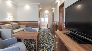 Hotellihuone, jossa on suuri litteänäyttöinen televisio, sohva, sohvapöytä ja kuviollinen matto.