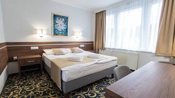 Ein Hotelzimmer mit Bett, Nachttischen, Schreibtisch, Stuhl, einem Fenster mit Vorhängen und einem Wandbild.