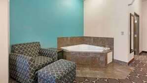 A bathroom with a bathtub, two patterned chairs, and a teal wall.