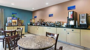 A hotel breakfast area with a self-serve coffee station, a refrigerator, and a buffet with various food items.