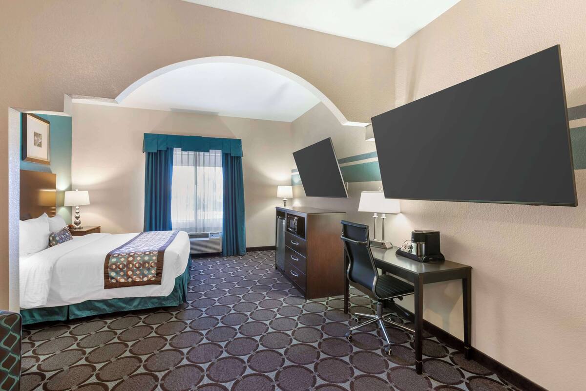 A hotel room with a bed, desk, chair, and a large TV.