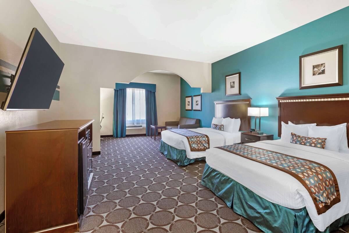 A hotel room with two beds, a desk, a TV, and a bathroom.