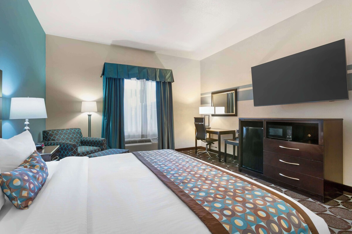 A hotel room with a large bed, a desk, a chair, a TV, and a minibar.