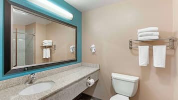 A bathroom with a granite countertop sink, a large mirror, a toilet, and a towel rack with folded towels.