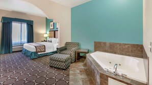 A hotel room with a bed, a sofa, a small table, a bathtub, and a patterned carpet.