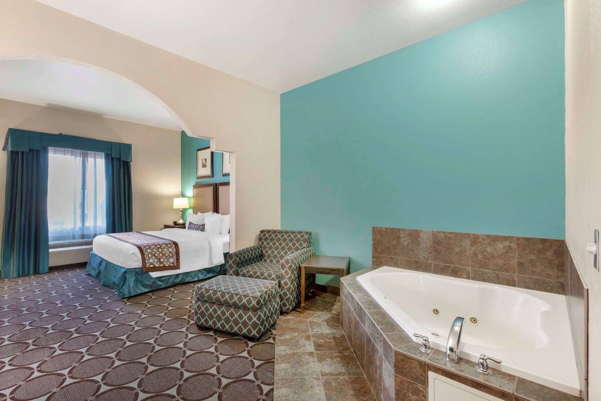 A hotel room with a bed, a sofa, a small table, a bathtub, and a patterned carpet.