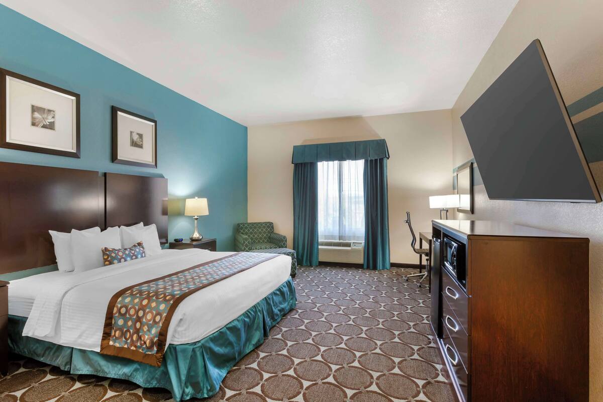 A hotel room with a large bed, a desk, a chair, a TV, and a window with curtains.