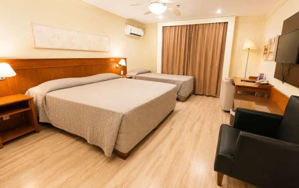 Habitación de hotel con dos camas, un escritorio, una silla, un televisor y un ventilador de techo.