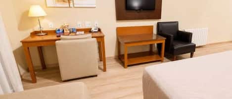 Una habitación de hotel con una cama, un escritorio, una silla, un televisor y obras de arte en la pared.