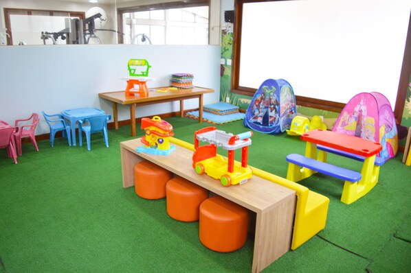 Una sala de juegos con alfombra verde, una mesa de madera, sillas coloridas y un tren de juguete.