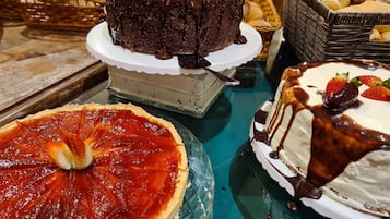Diversos doces em exposição, incluindo um bolo de chocolate, uma tarte de morango e um bolo branco com calda de chocolate e morangos.