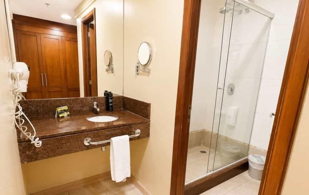 A bathroom with a marble countertop, a sink, a mirror, and a glass-enclosed shower.