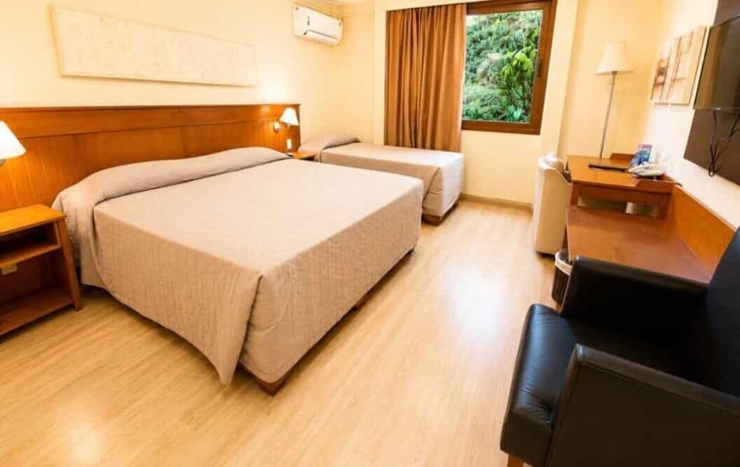 Habitación de hotel con dos camas, un escritorio, una silla y una ventana con cortinas.
