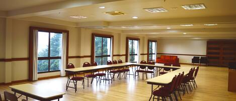 A large conference room with multiple tables and chairs, large windows, and a wooden floor.