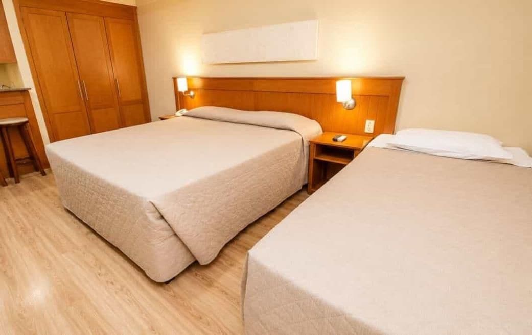 Et hotelværelse med to senge, et træskab, sengeborde og vægmonterede lamper.