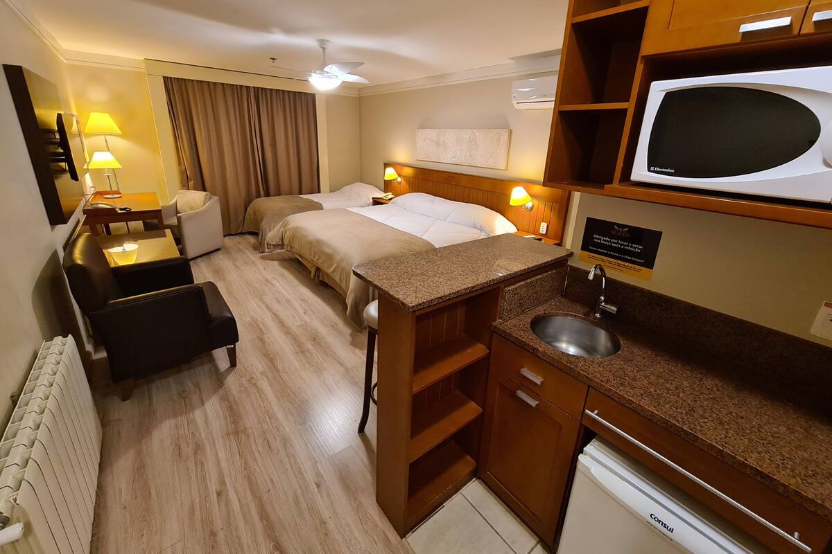 A hotel room with two beds, a desk, a chair, a microwave, a sink, and a radiator.