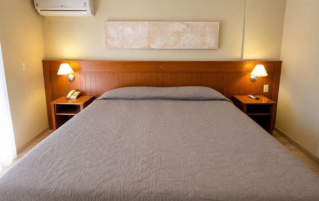 Una habitación de hotel con una cama grande, dos mesitas de noche con lámparas, un teléfono y aire acondicionado de pared.