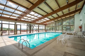 An indoor swimming pool with a view of the outdoors, wooden beams, and tiled flooring. - Sky Borges Hotel Alpenhaus (Gramado)