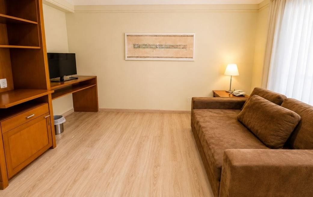 A hotel room with a wooden desk, a television, a sofa, a lamp, and a painting on the wall.