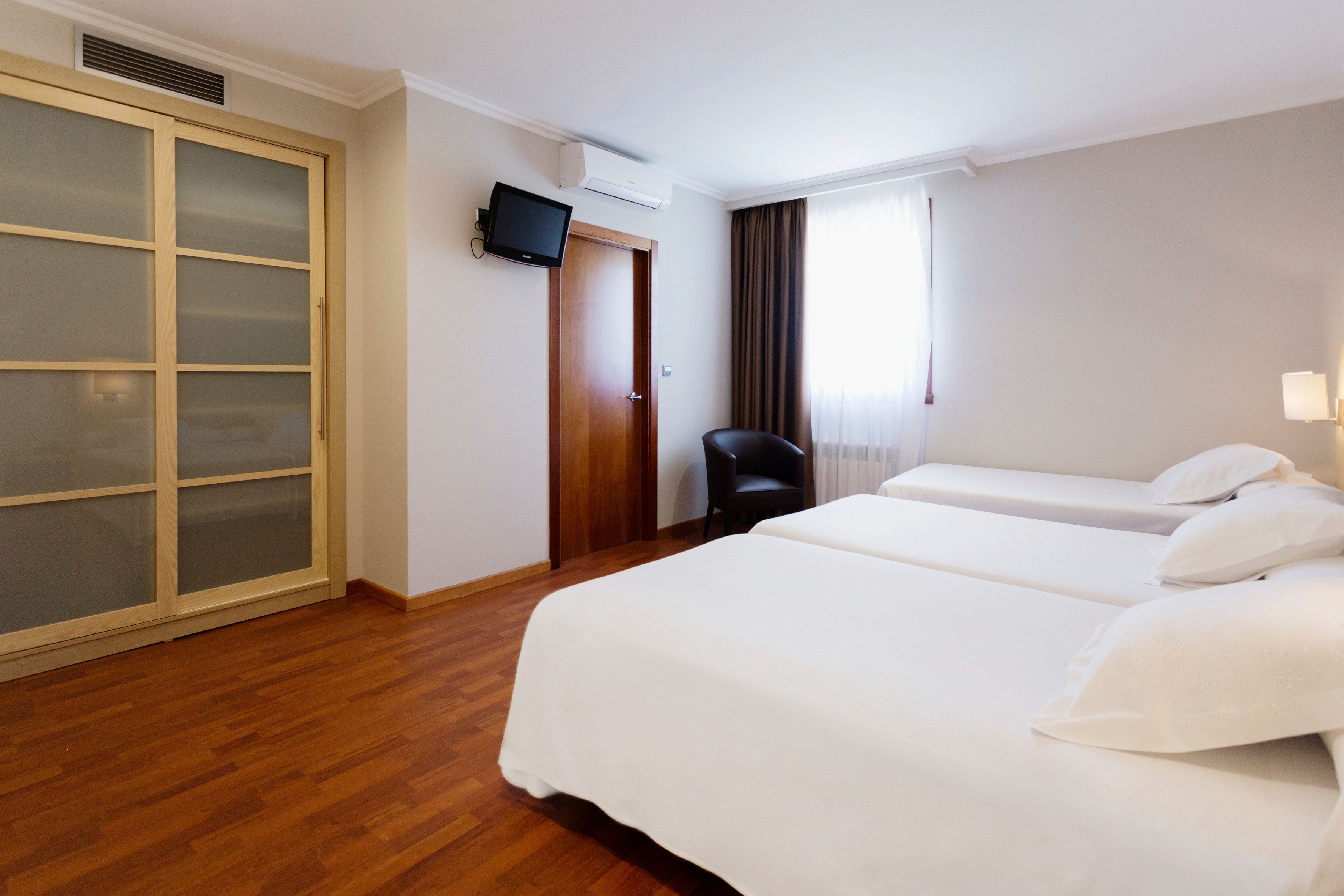 A hotel room with two beds, a wardrobe, a television, and a chair.