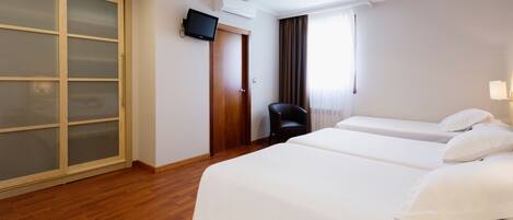 A hotel room with two beds, a wardrobe, a television, and a chair.