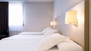 A hotel room with two beds, a nightstand, a lamp, and a view of the outdoors.