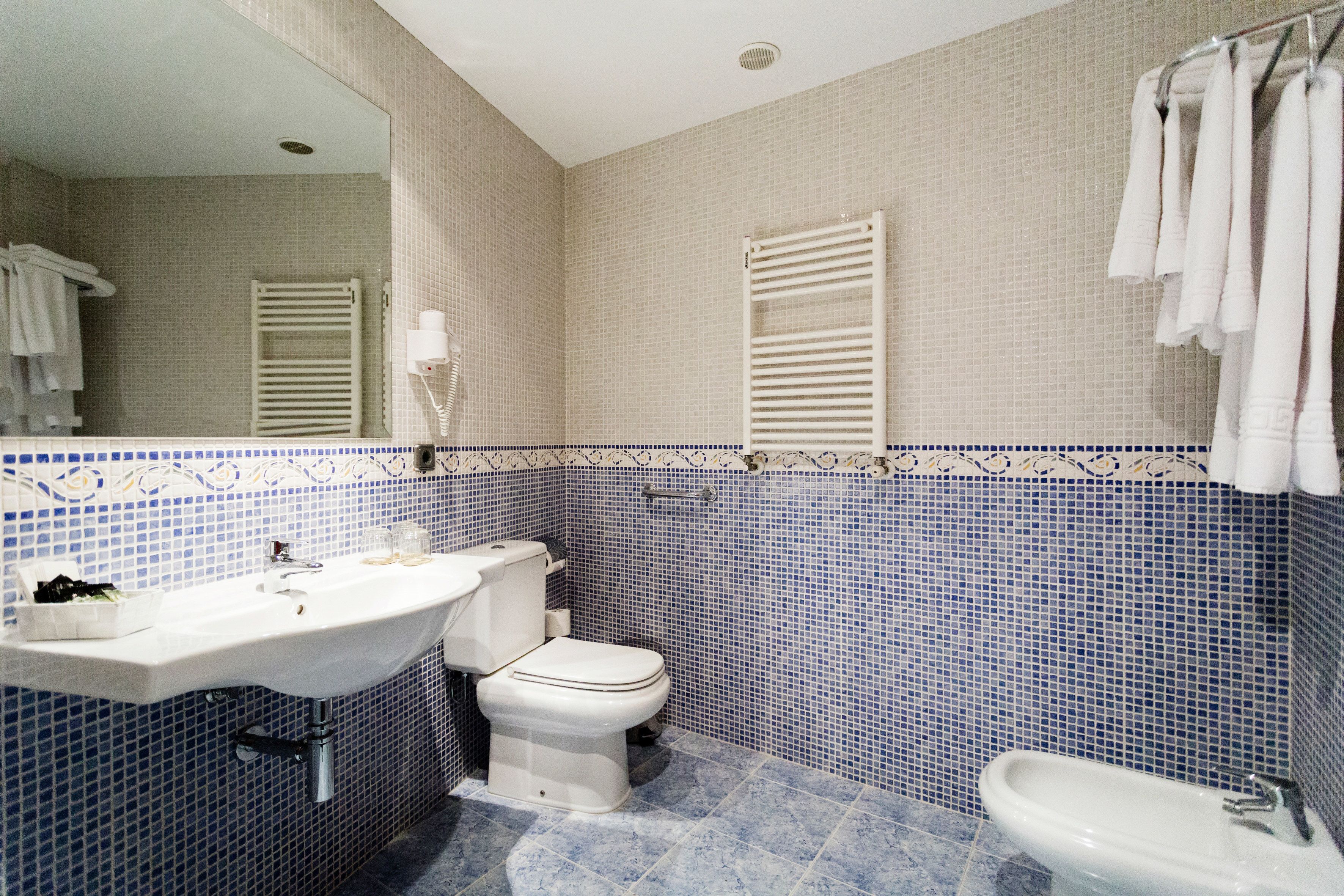 Un baño con lavamanos, inodoro y bidé blancos, con azulejos en azul y beige.