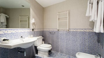 Un baño con lavamanos, inodoro y bidé blancos, con azulejos en azul y beige.