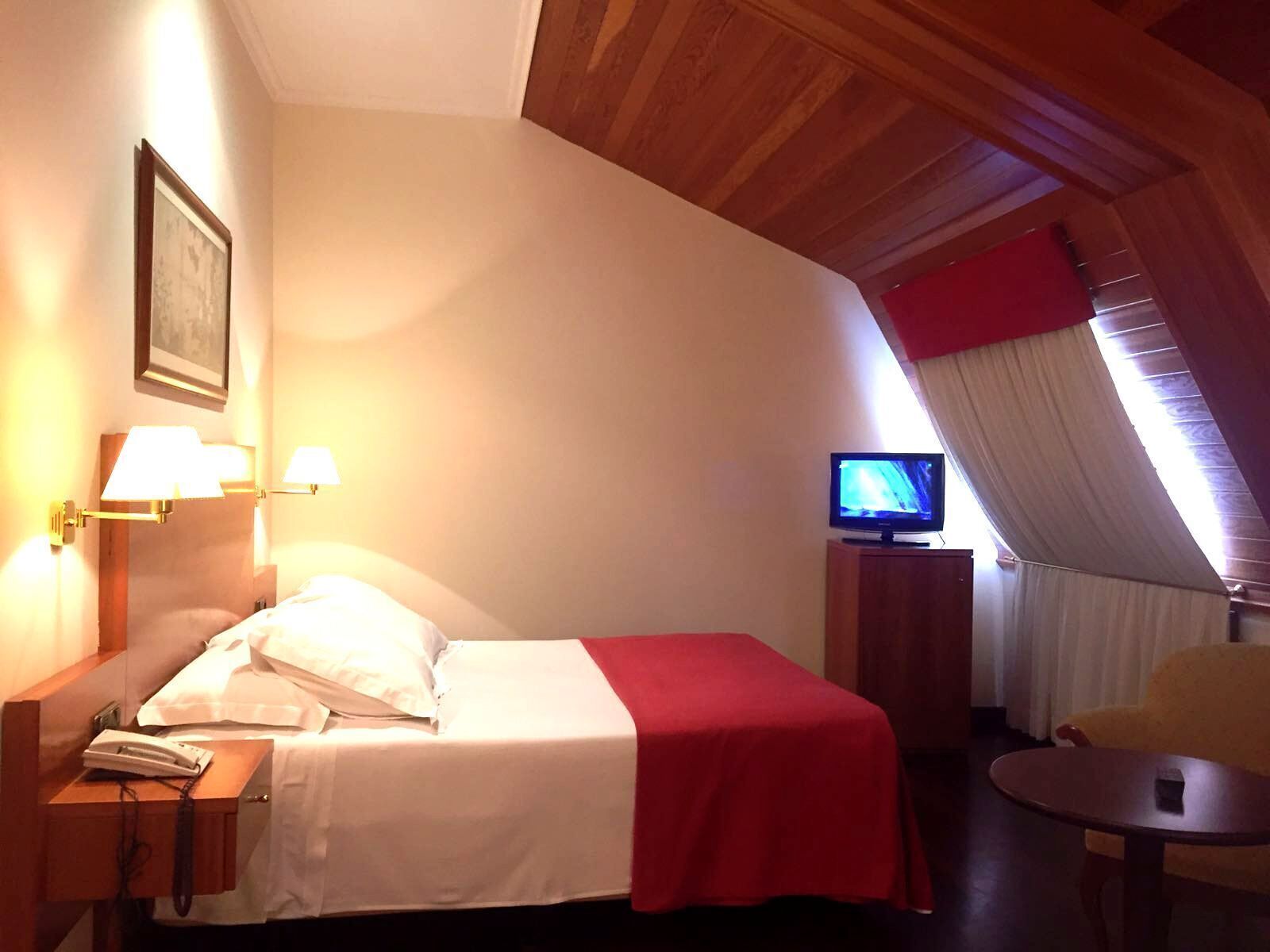 A hotel room with a bed, a television, a chair, and a desk with a telephone.