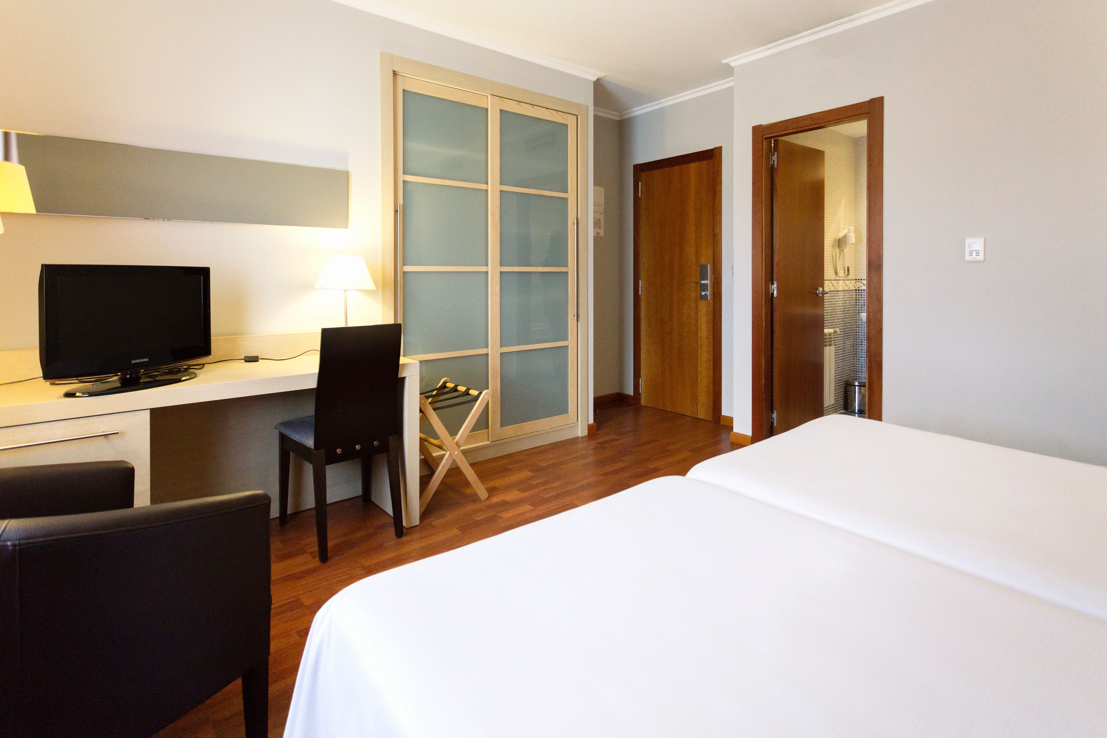 Habitación de hotel con una cama, un escritorio con computadora y silla, un televisor y un armario.