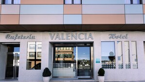 L'ingresso di un hotel con una facciata moderna, con il nome 'Valencia Hotel' ben visibile e il riflesso dell'edificio sulle vetrate.