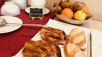 A breakfast setting with croissants, a pitcher of milk, a basket of fruits, and a sign indicating 'leche desnatada'.