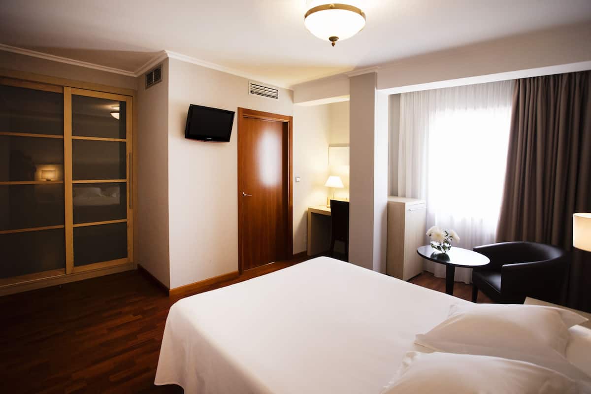 A hotel room with a bed, a desk, a chair, a TV, and a window with curtains.