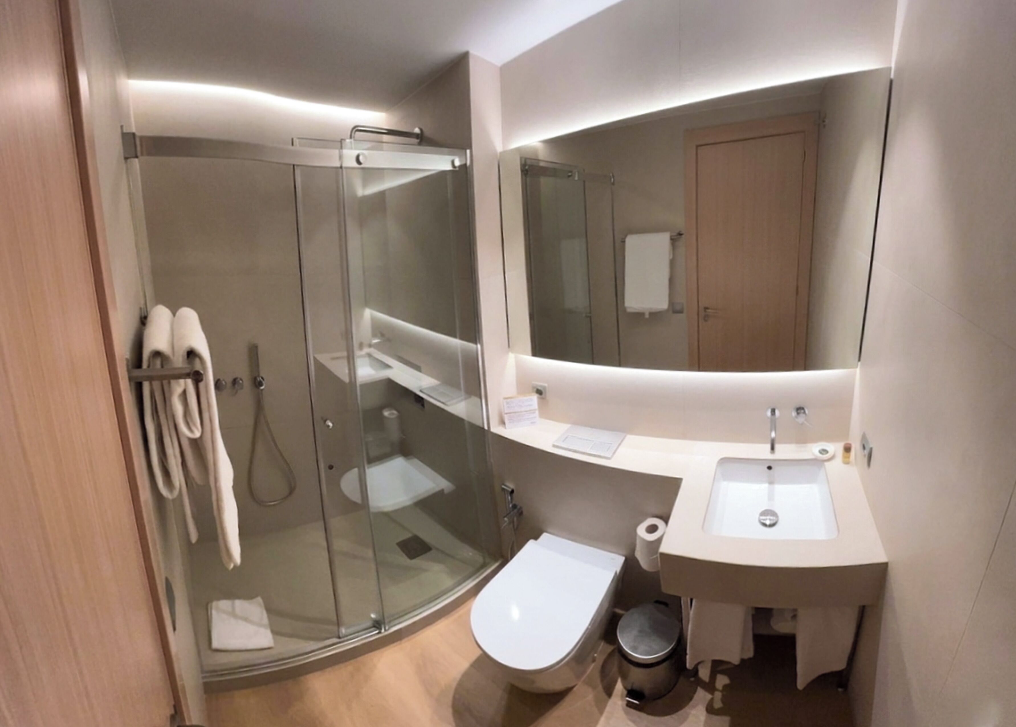 Un baño moderno con ducha de vidrio, inodoro, lavabo y espejo.