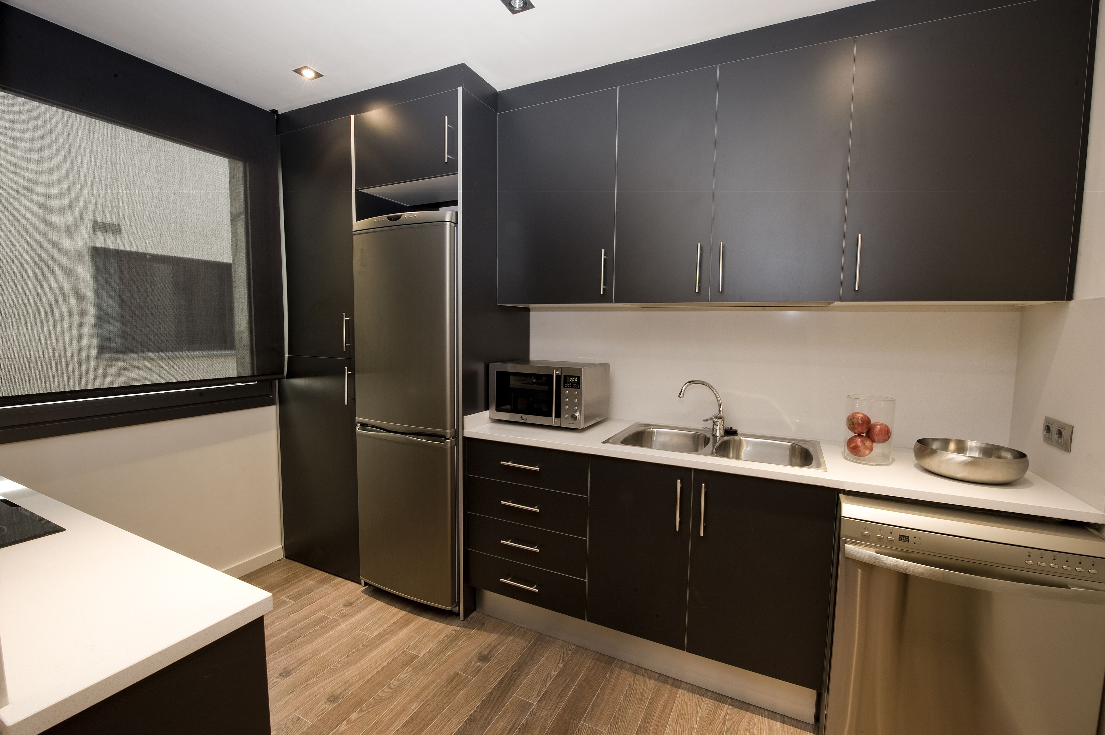 Een moderne keuken met donkere kastjes, roestvrijstalen apparatuur en een wit aanrecht.