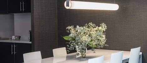 A modern dining area with a white table, four chairs, a vase with flowers, and a pendant light.