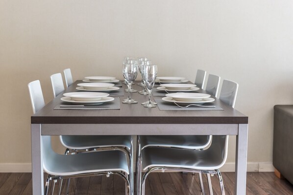 Une table à manger dressée avec des assiettes, des couverts et des verres à vin, entourée de chaises modernes.