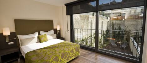 A hotel room with a large bed, a nightstand, a lamp, and a view of the outside balcony.