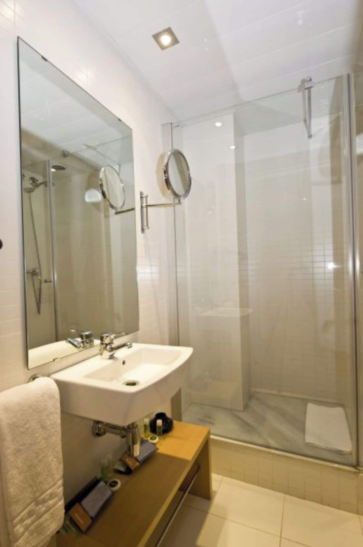 Une salle de bain moderne avec une douche à parois de verre, un grand miroir et un lavabo blanc.