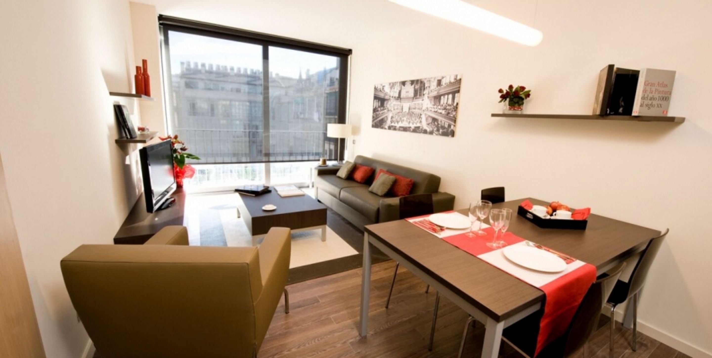A modern living room with a sofa, a dining table set for two, and a large window offering a city view.