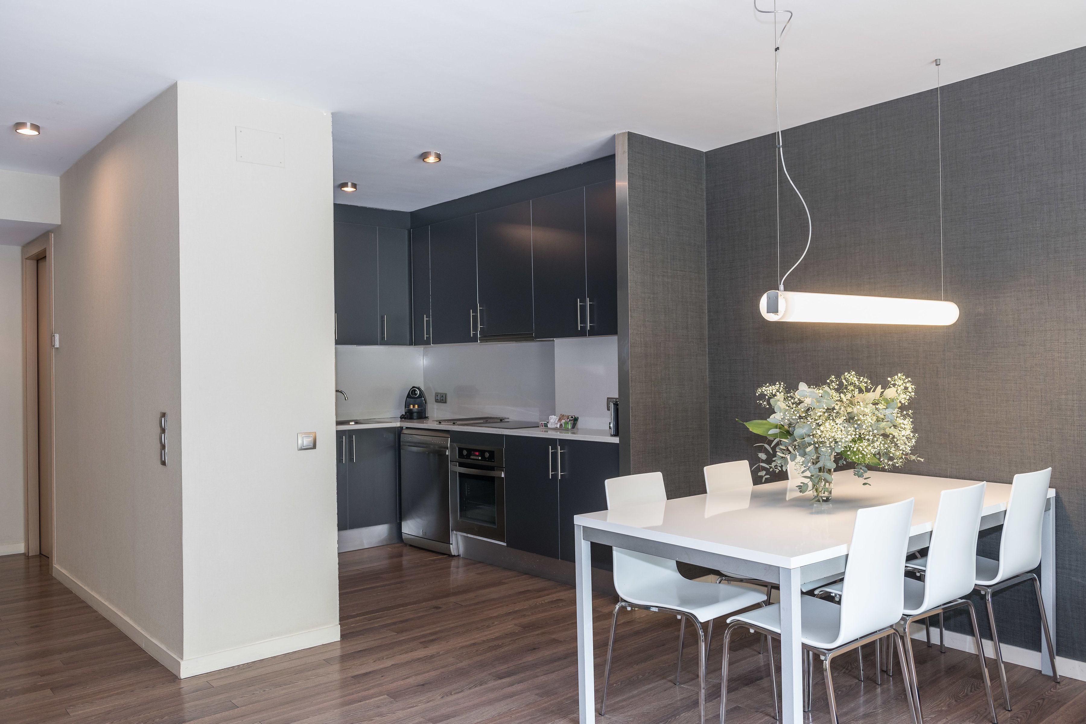 Una cocina moderna con armarios oscuros, una mesa de comedor blanca y una lámpara colgante.