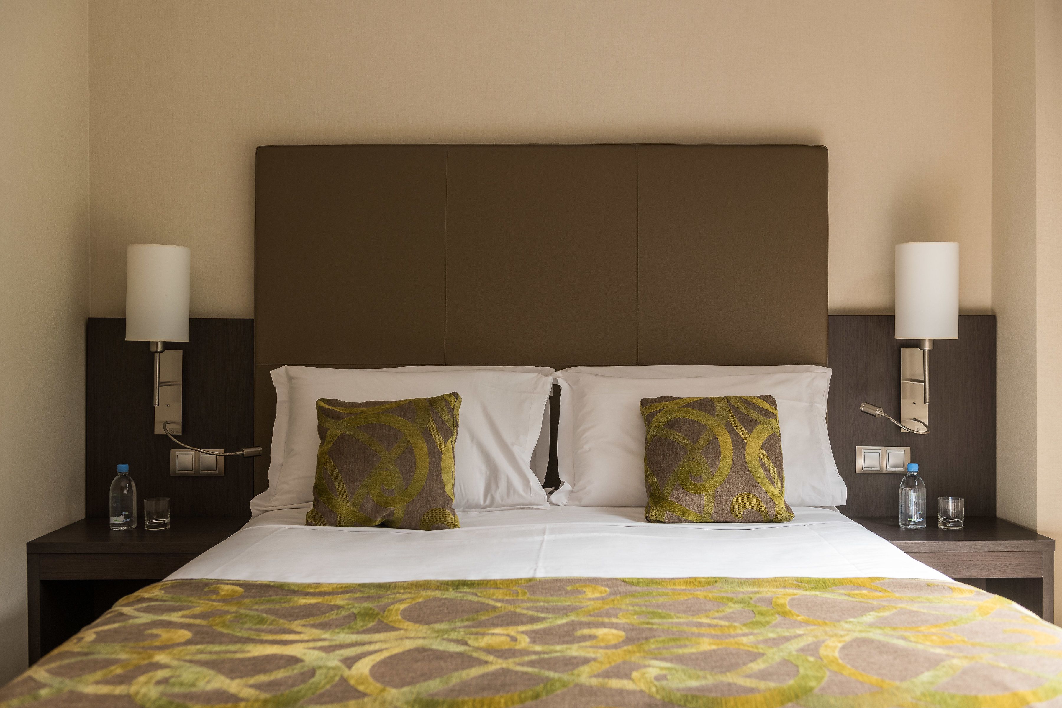 A hotel room with a large bed, two pillows, two bedside tables, and two wall-mounted lamps.