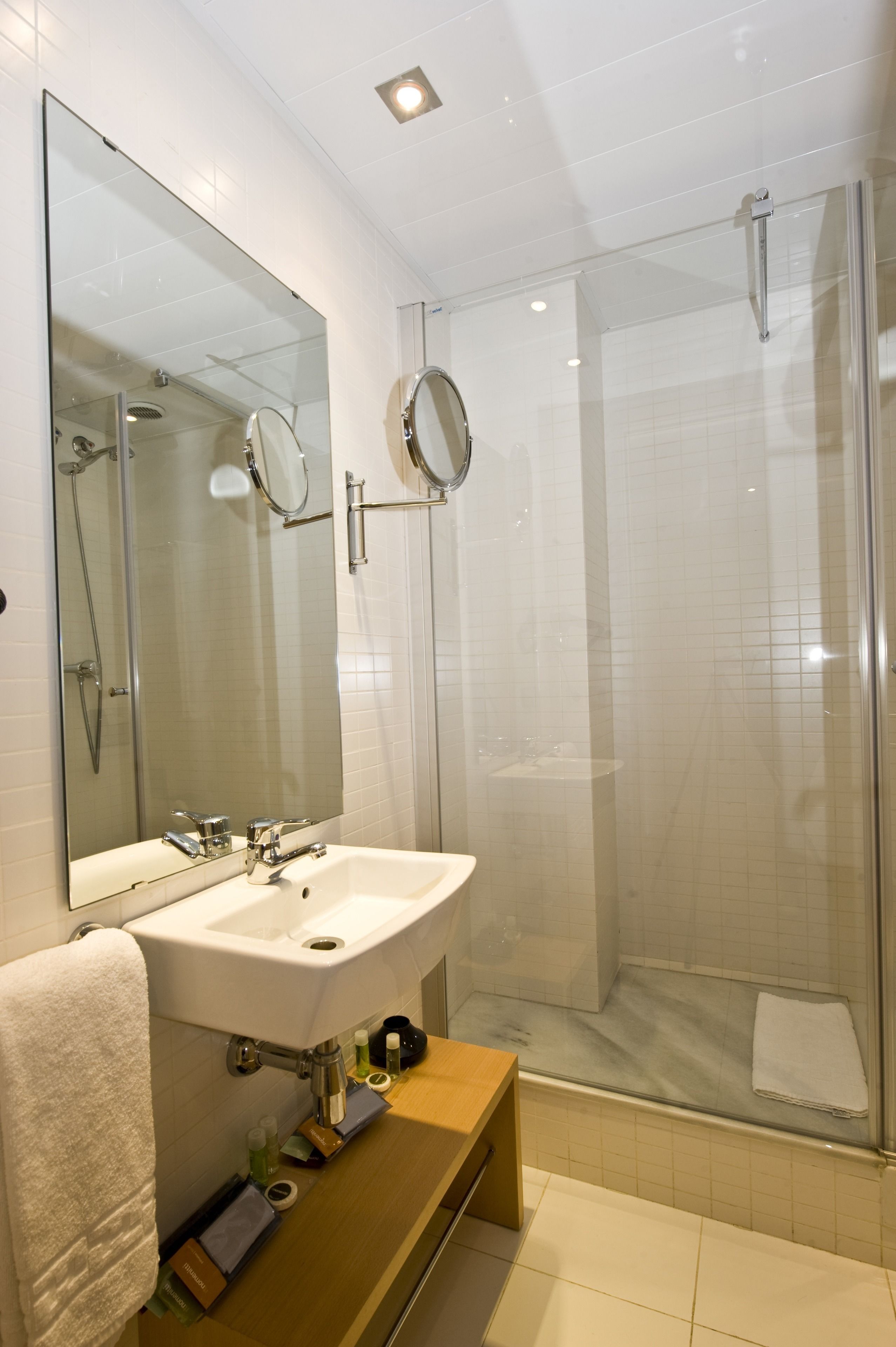 A modern bathroom with a large mirror, a sink, and a glass-enclosed shower.