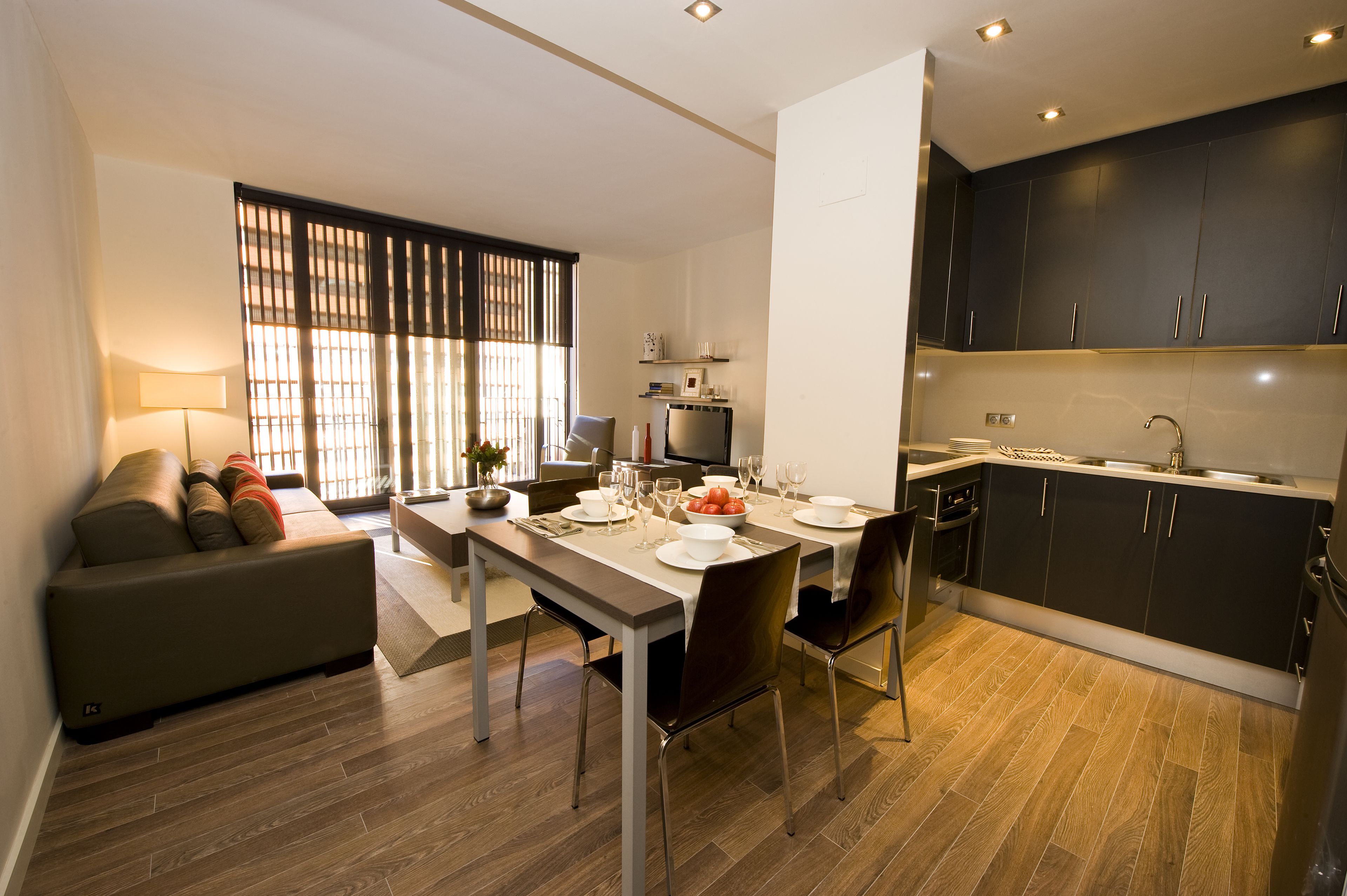 Un salon moderne comprenant un canapé, une table à manger et un coin cuisine avec des meubles sombres et un plancher en bois.