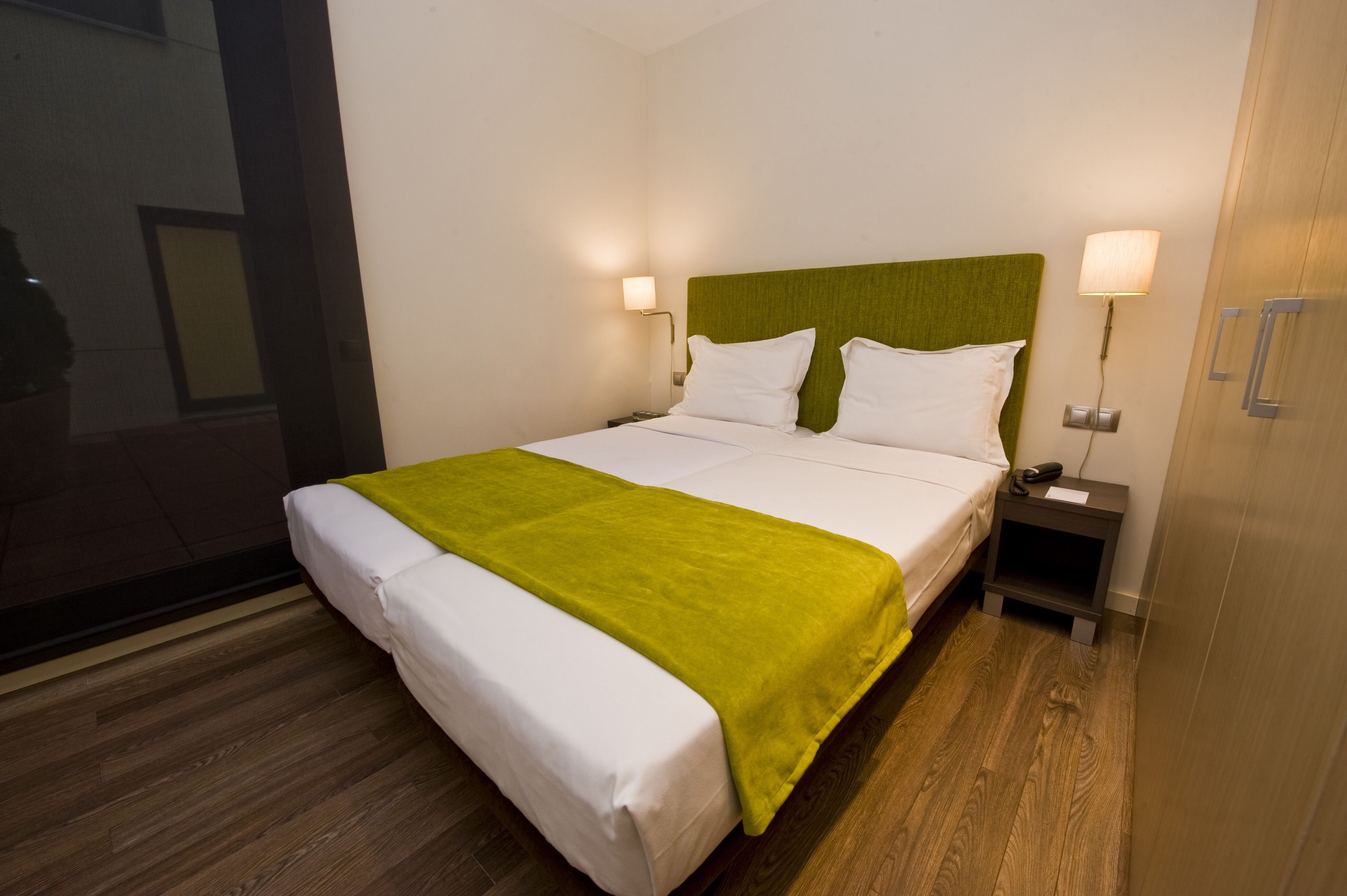 Ein Hotelzimmer mit Bett, grünem Kopfteil, zwei Nachttischlampen, einem Nachttisch und Holzboden.