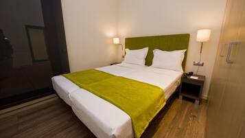 Ein Hotelzimmer mit Bett, grünem Kopfteil, zwei Nachttischlampen, einem Nachttisch und Holzboden.