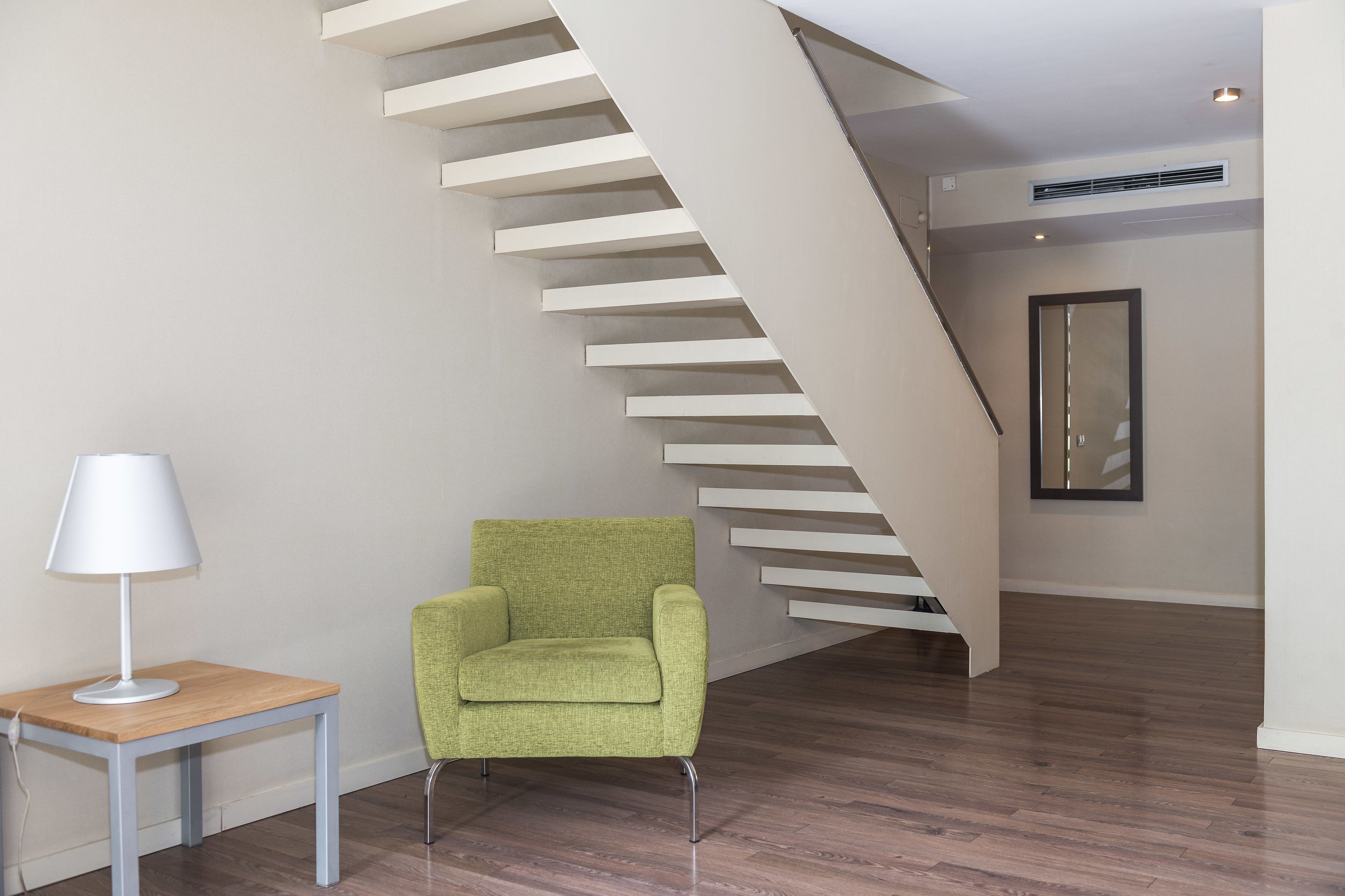 A modern interior with a staircase, a green armchair, and a small table with a lamp.