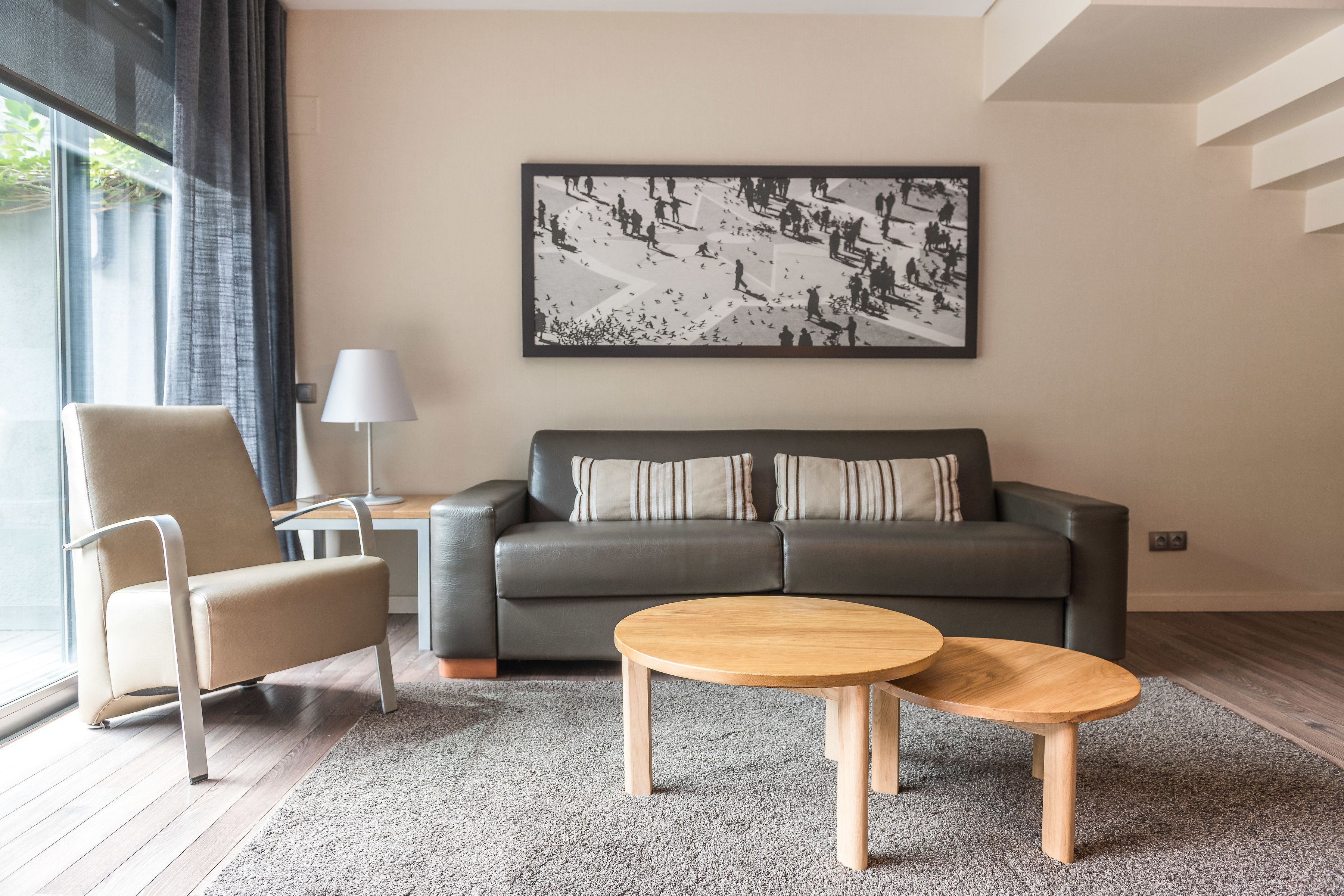 Una sala de estar moderna con un sofá gris, un sillón color beige y dos mesas de centro de madera.