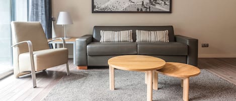 Una sala de estar moderna con un sofá gris, un sillón color beige y dos mesas de centro de madera.
